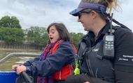 A woman with learning difficulties driving a powerboat with an instructor alongside, on the River Thames