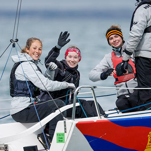 3 smiling young people posing a and waving at the camera on the back of a keel boat