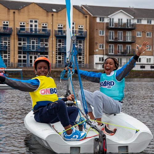 Two happy children smiling on a pico sail boat on the water