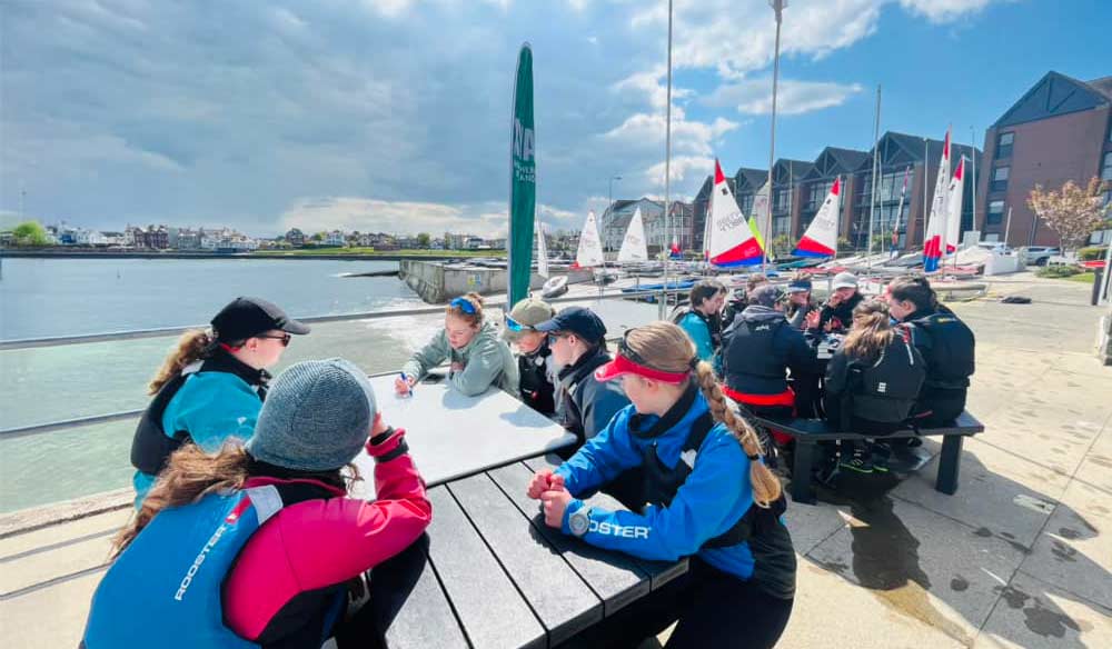  a group of children sitting  round a table outside Ballyholme sailing club in northern Ireland