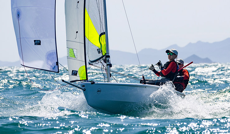 Teenagers Ben Greenhalgh and Tom Sinfield from Port Dinorwic Sailing Club sending it downwind with the kite flying on the sea and in the sunshine at the 2023 RS Feva Worlds in Italy.