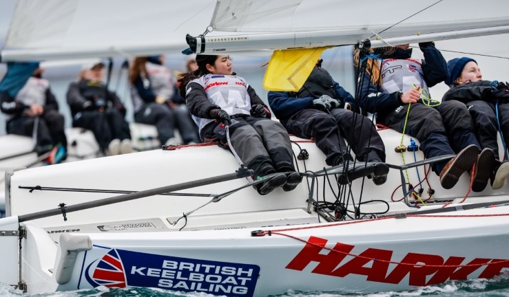 Close up photograph of a team sailing an Elliott 6M keelboat upwind with another team in the background and directly alongside while competing at an RYA women's match racing event.