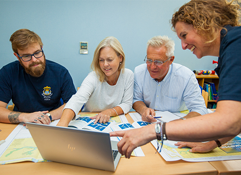 Group of adults sat around laptop with charts and training materials