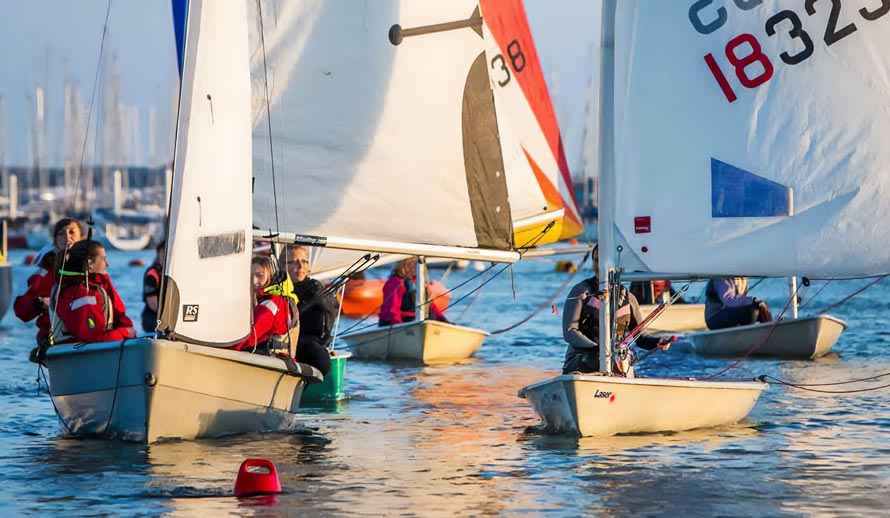 Mid shot of 4 dingy boats with sailors sailing out of a mariner 